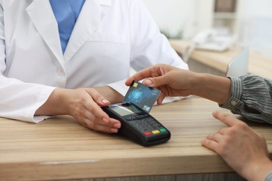 Receptionist taking payment from client via terminal at hospital, closeup