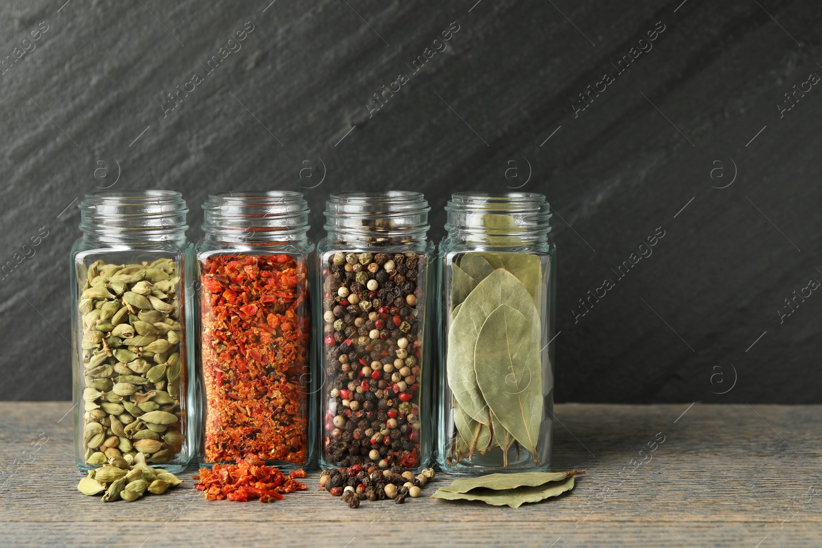 Photo of Different spices in glass jars on grey wooden table, closeup. Space for text