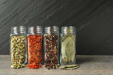 Different spices in glass jars on grey wooden table, closeup. Space for text