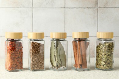 Photo of Different spices in glass jars on light textured table, closeup