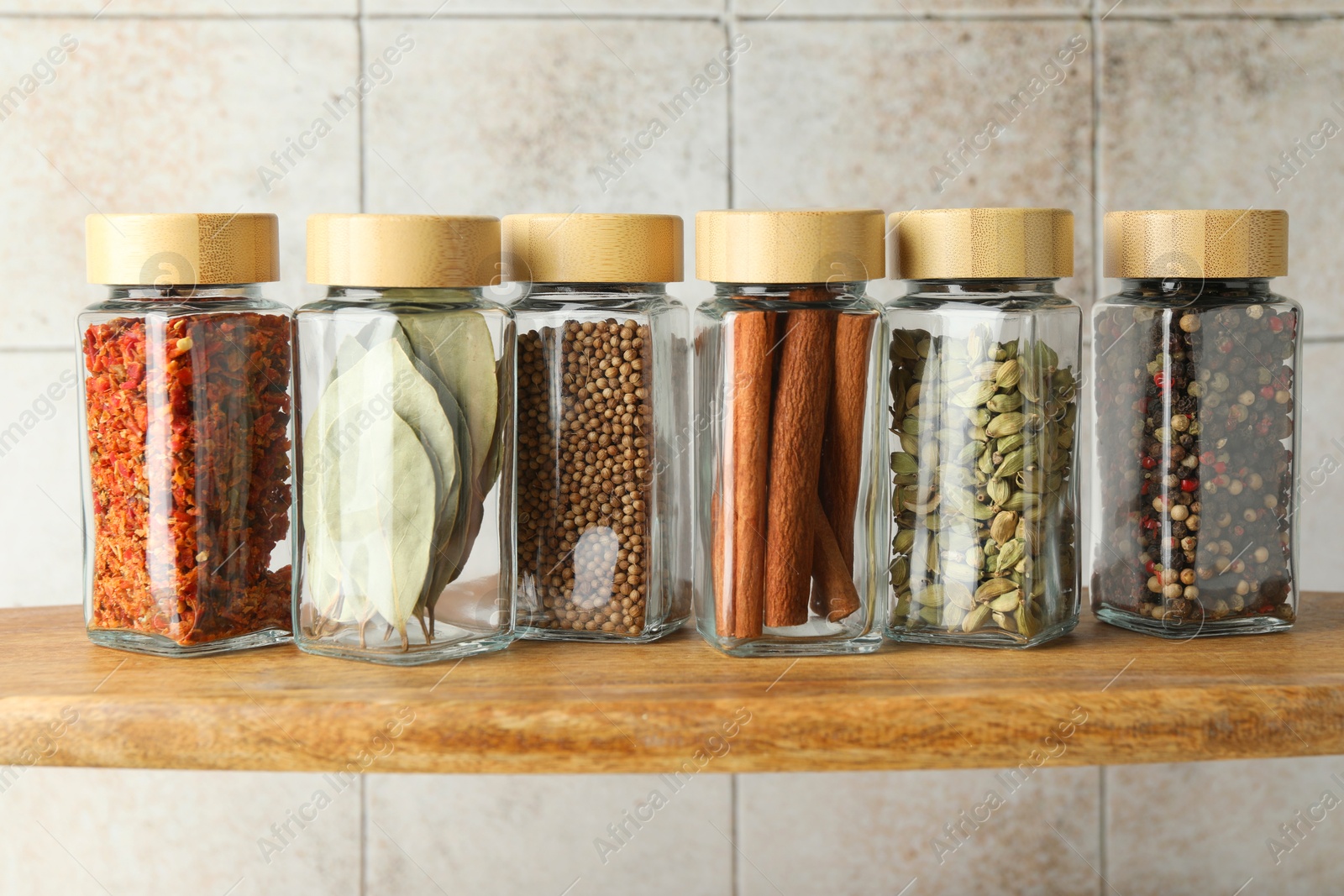 Photo of Different spices in glass jars on wooden shelf, closeup