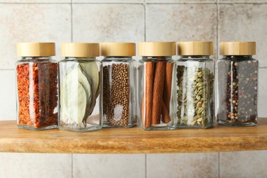 Different spices in glass jars on wooden shelf, closeup