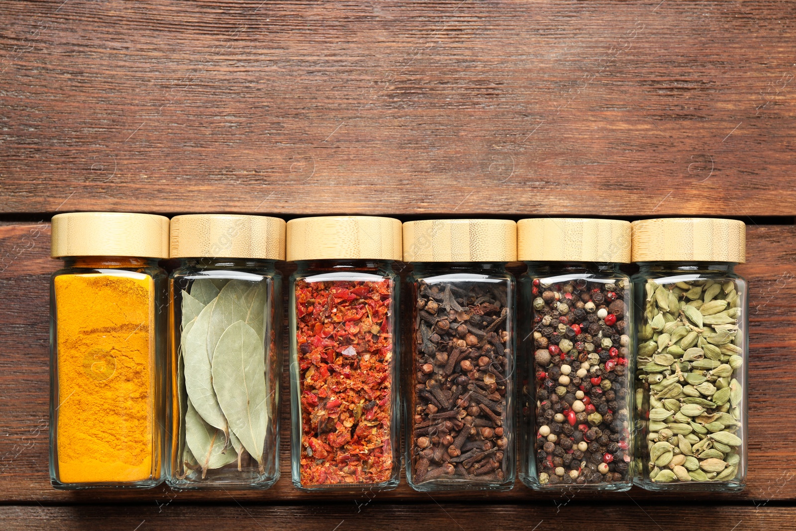 Photo of Different spices in glass jars on wooden table, top view