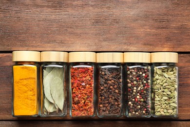 Different spices in glass jars on wooden table, top view