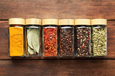 Photo of Different spices in glass jars on wooden table, top view