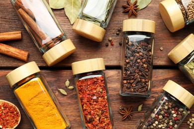 Different spices in glass jars on wooden table, flat lay