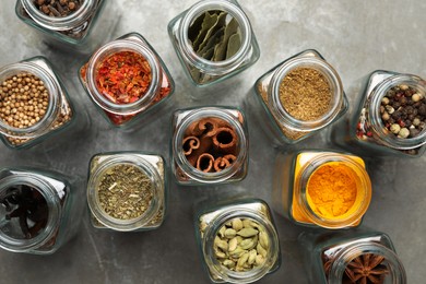 Photo of Different spices in glass jars on grey table, flat lay