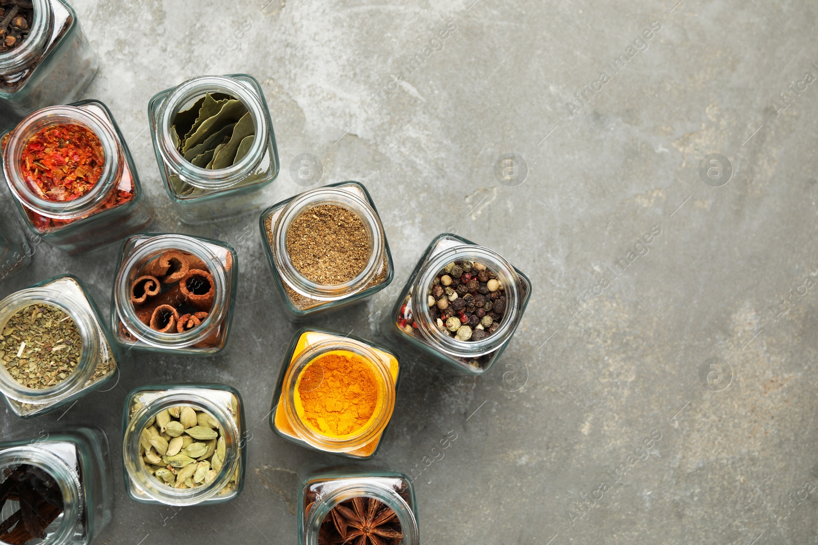 Photo of Different spices in glass jars on grey table, flat lay. Space for text