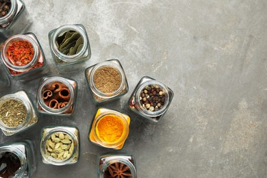 Different spices in glass jars on grey table, flat lay. Space for text