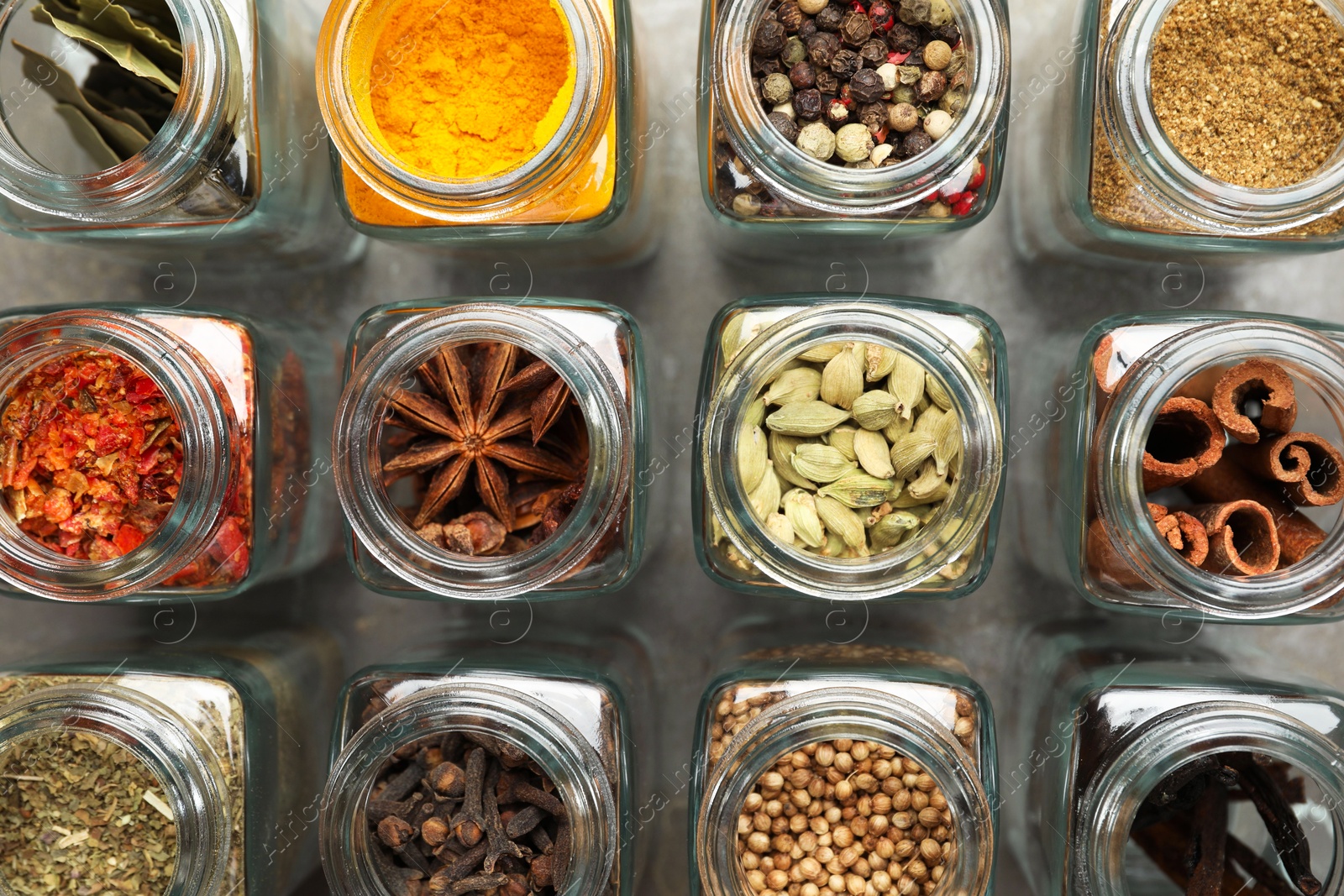 Photo of Different spices in glass jars on grey table, flat lay