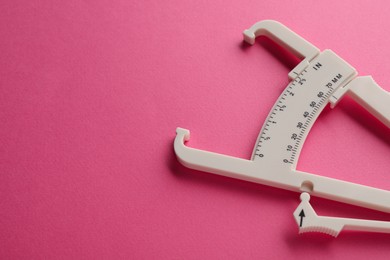 Photo of Plastic body fat caliper on pink background, closeup. Space for text