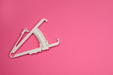 Photo of Plastic body fat caliper on pink background, top view. Space for text