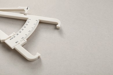 Photo of Plastic body fat caliper on grey background, closeup. Space for text