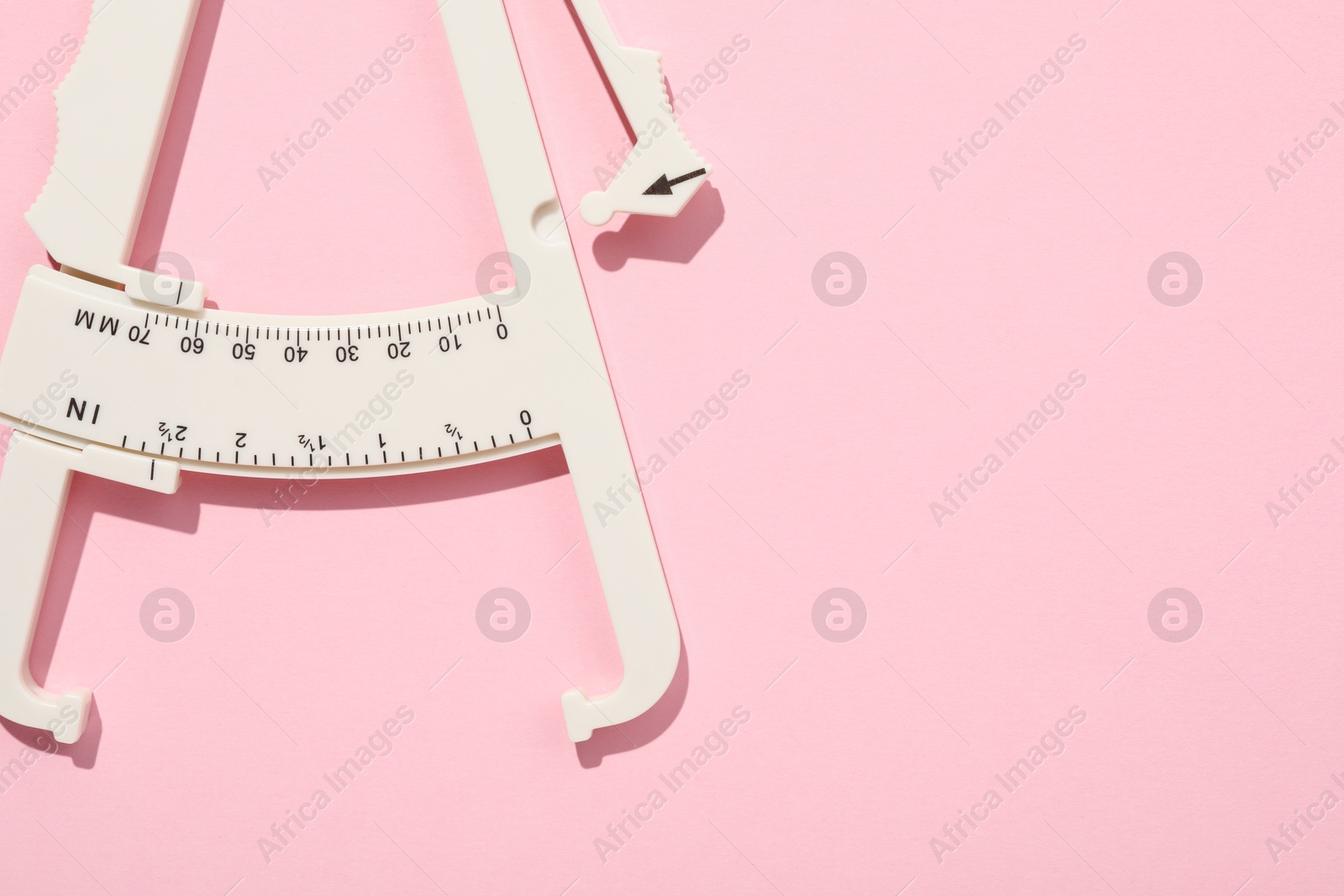 Photo of Plastic body fat caliper on pink background, top view. Space for text