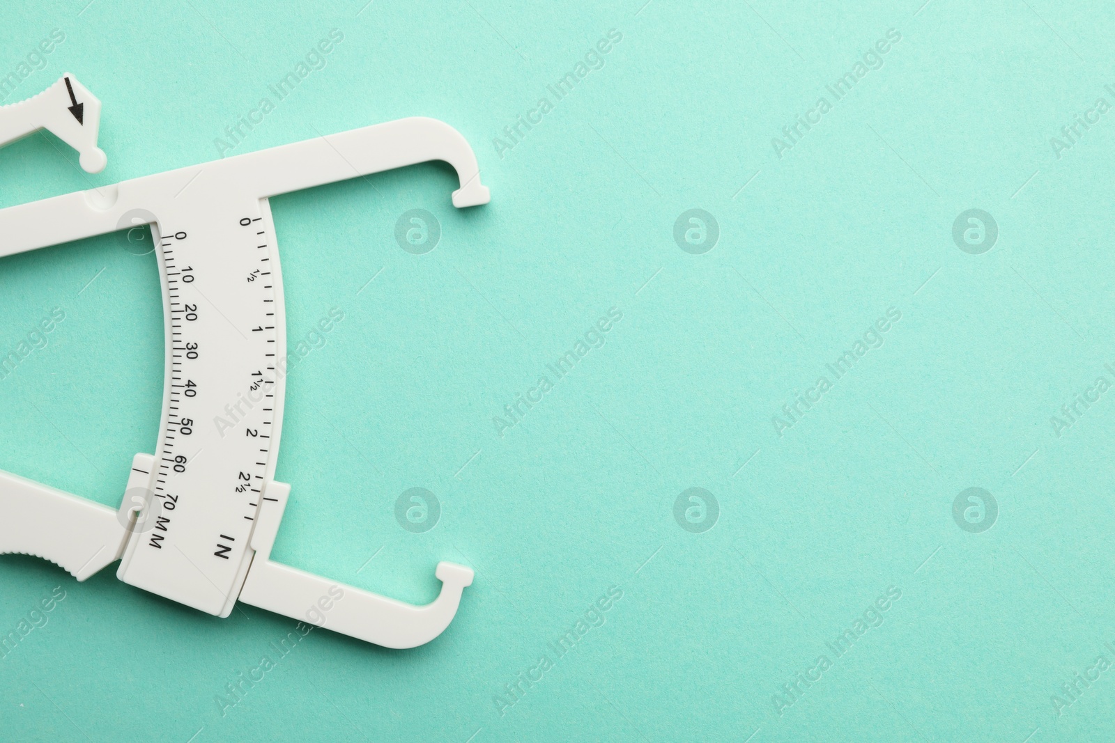 Photo of Plastic body fat caliper on turquoise background, top view. Space for text