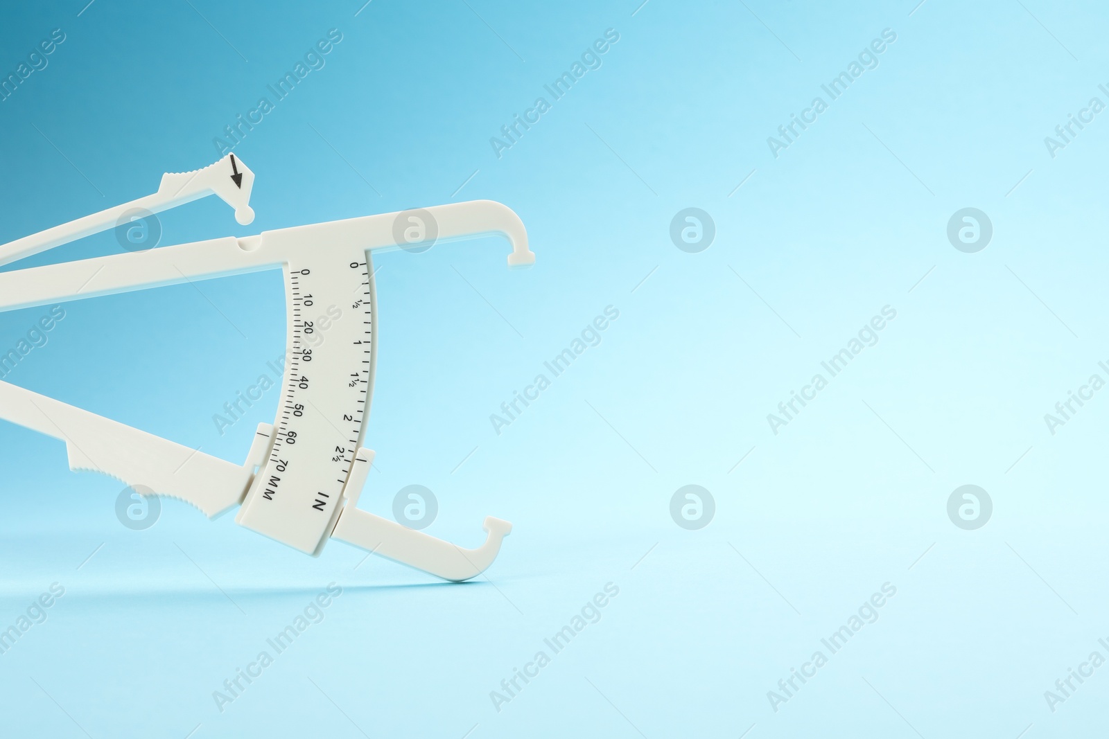 Photo of Plastic body fat caliper on light blue background. Space for text