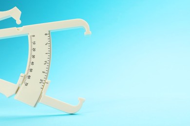 Photo of Plastic body fat caliper on light blue background. Space for text