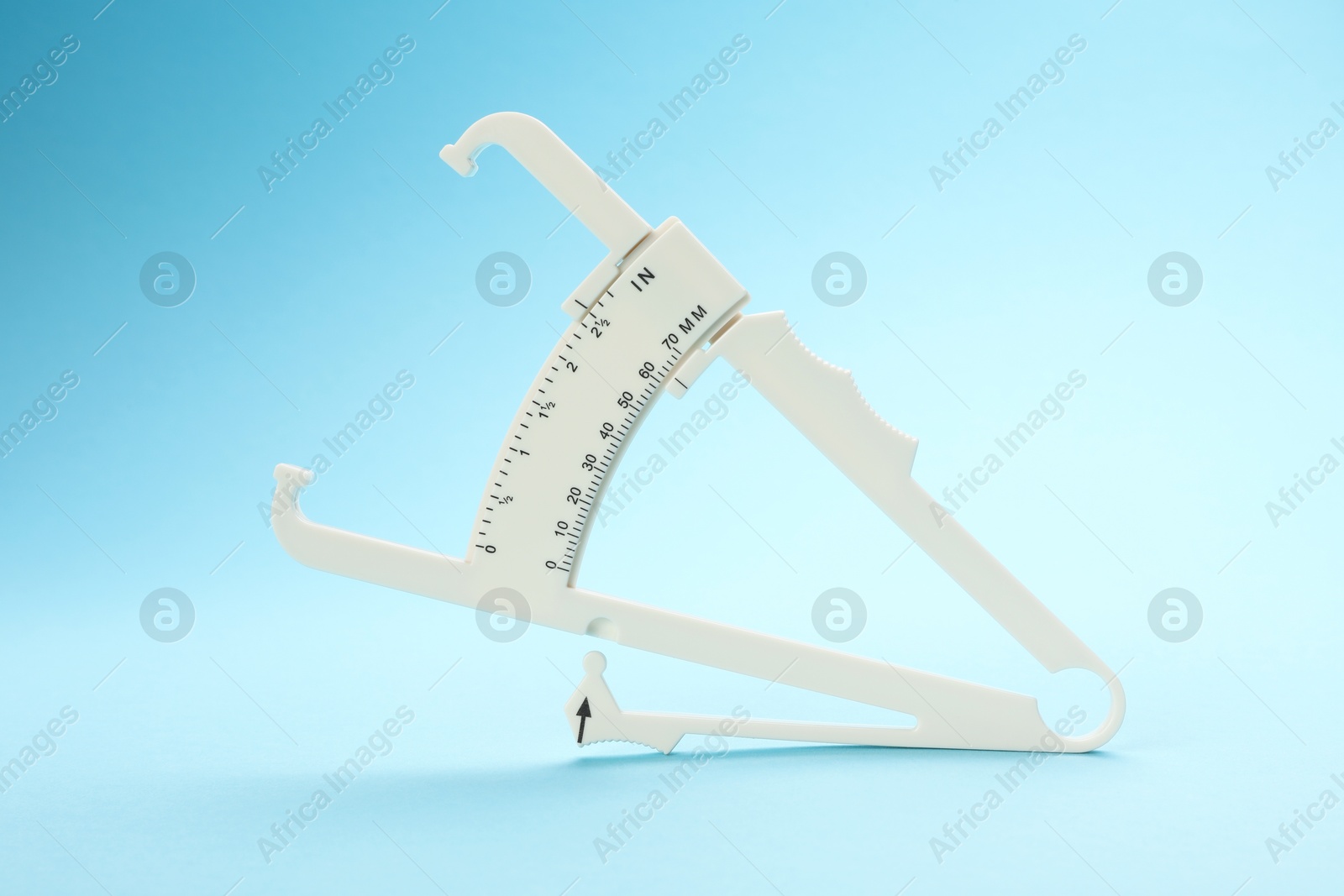 Photo of Plastic body fat caliper on light blue background