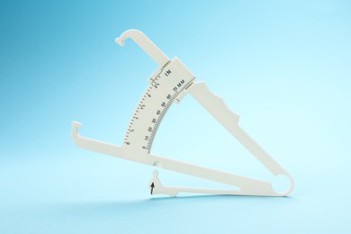 Photo of Plastic body fat caliper on light blue background