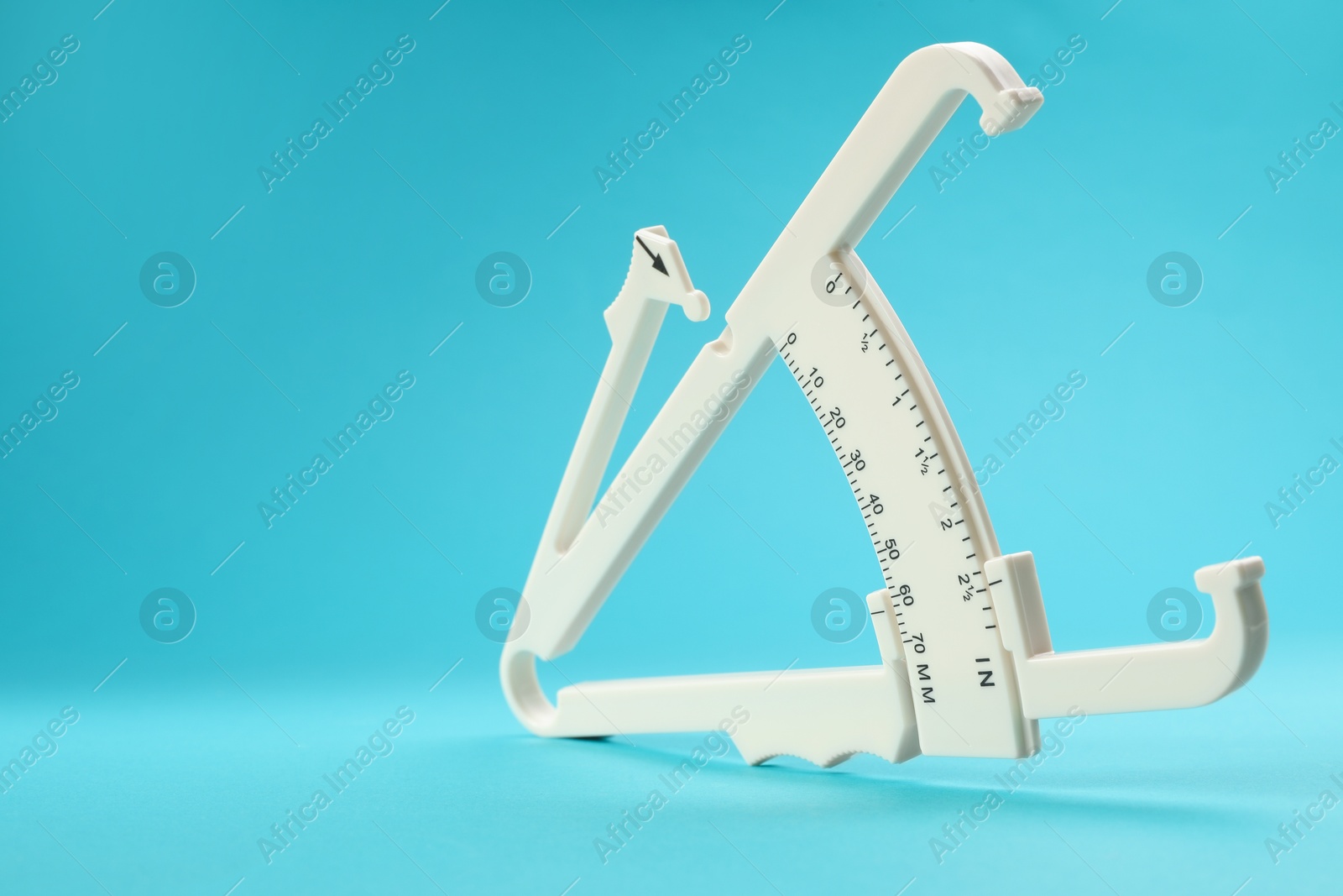 Photo of Plastic body fat caliper on light blue background, closeup