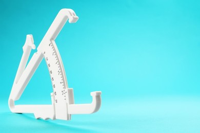 Photo of Plastic body fat caliper on light blue background, closeup. Space for text