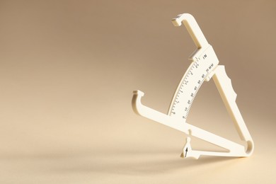 Photo of Plastic body fat caliper on beige background. Space for text