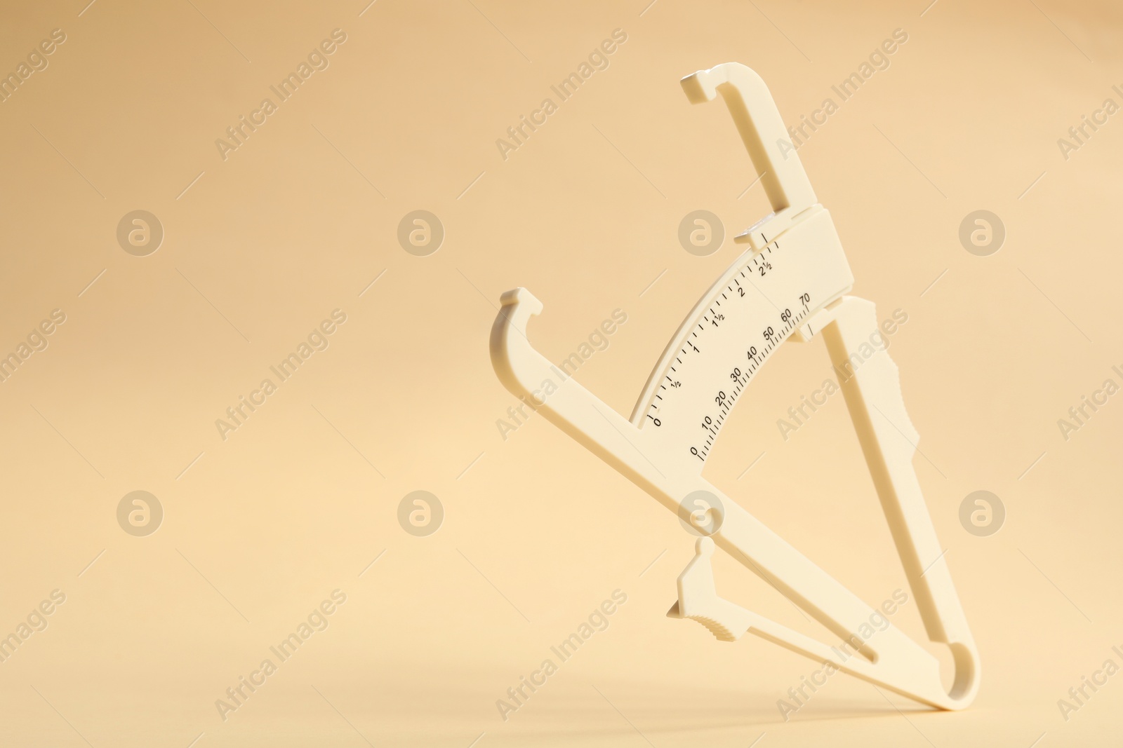 Photo of Plastic body fat caliper on beige background. Space for text