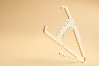 Photo of Plastic body fat caliper on beige background. Space for text