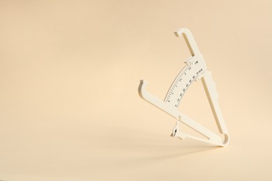 Photo of Plastic body fat caliper on beige background. Space for text