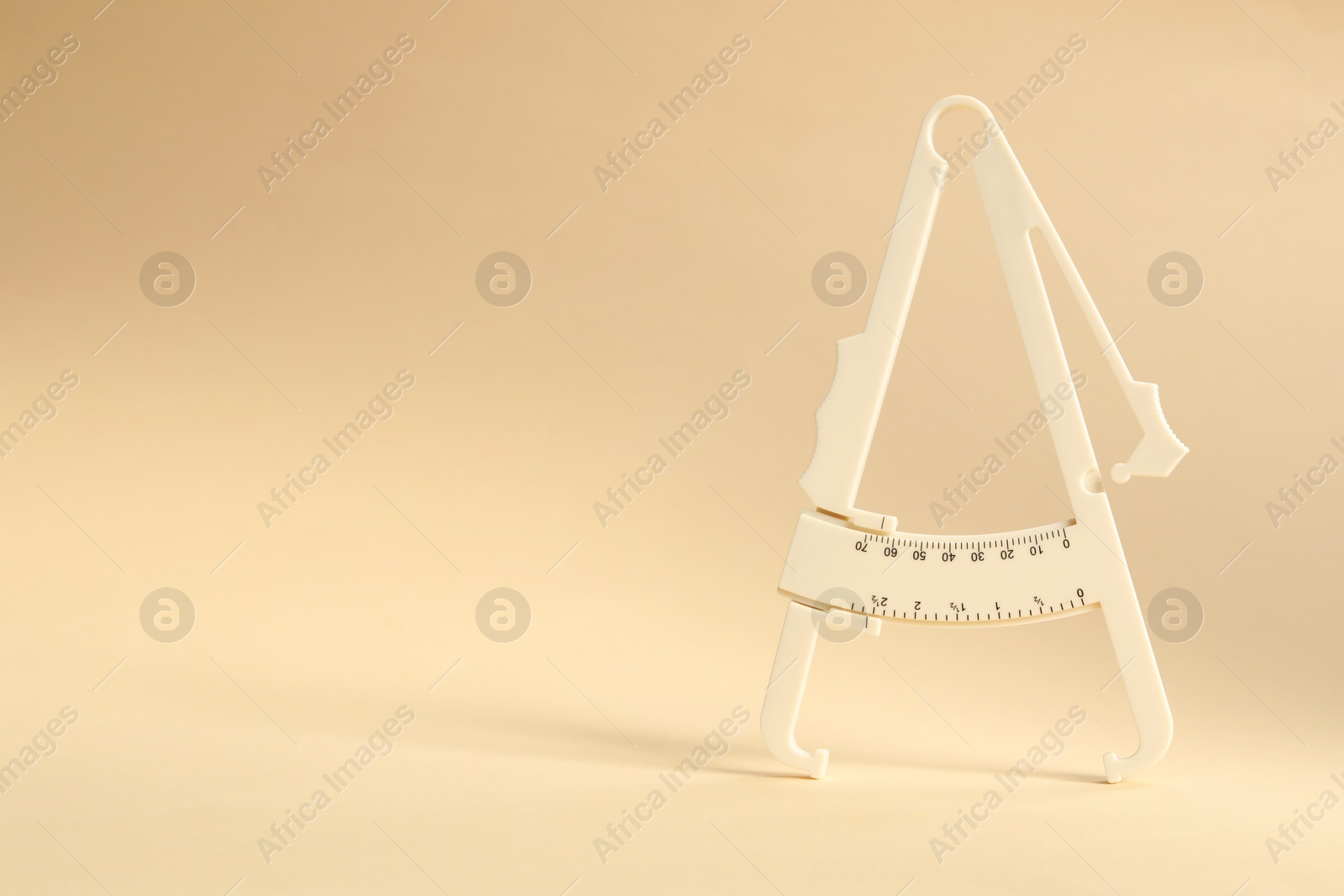 Photo of Plastic body fat caliper on beige background. Space for text