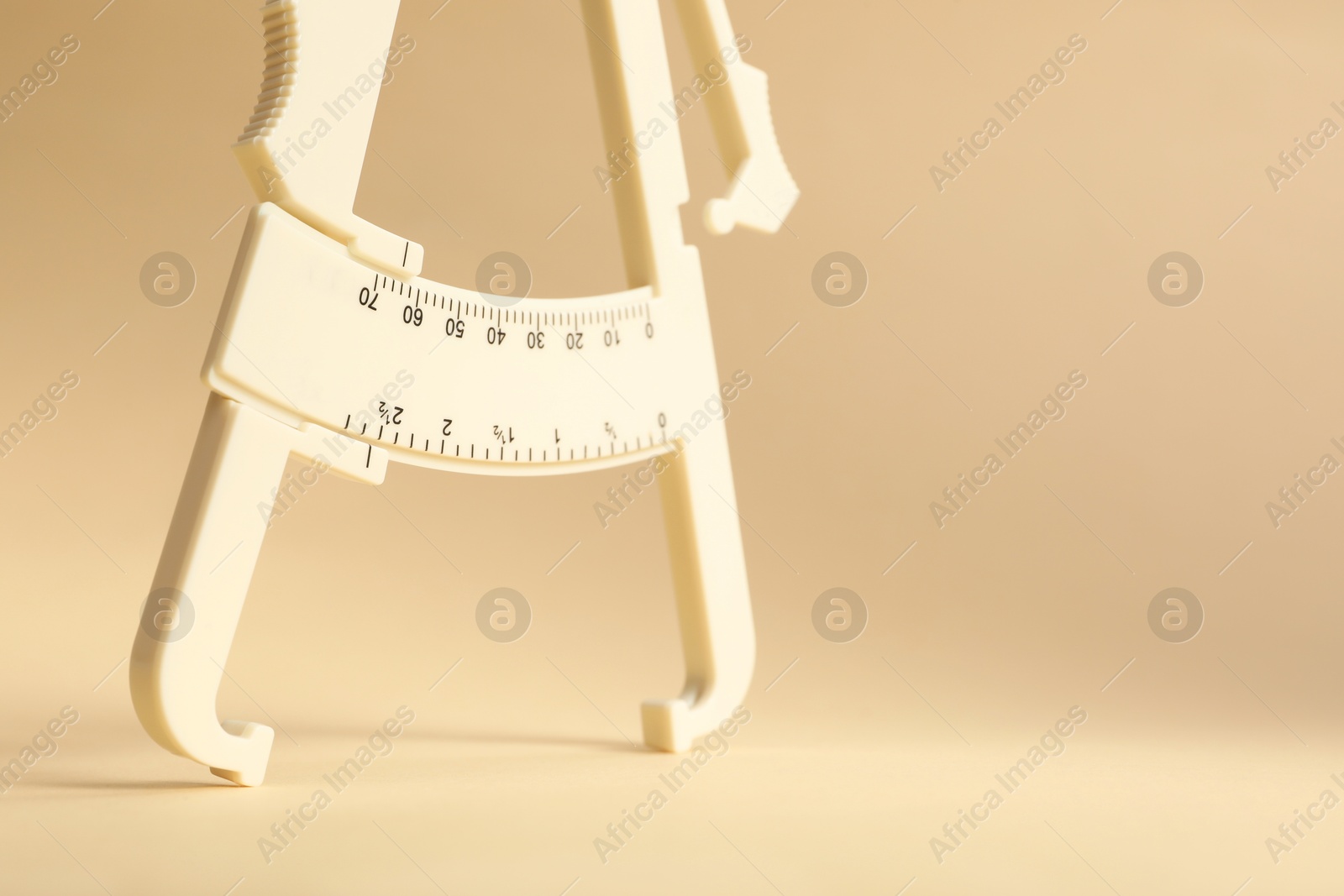 Photo of Plastic body fat caliper on beige background, closeup. Space for text