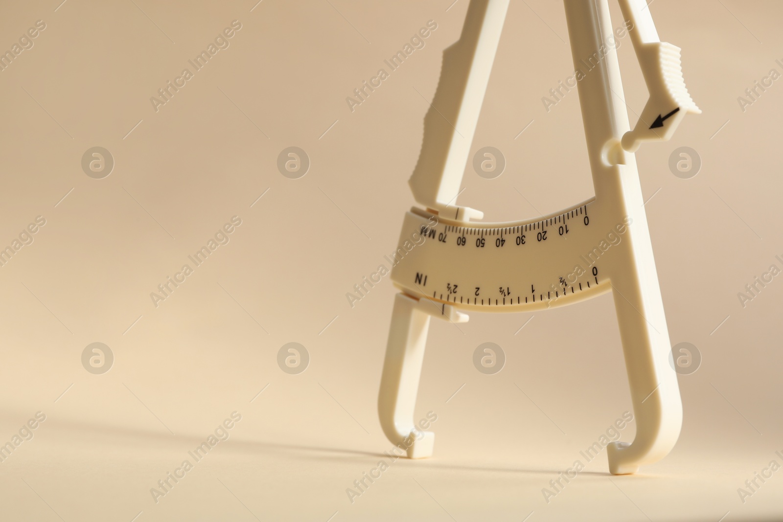 Photo of Plastic body fat caliper on beige background, closeup. Space for text