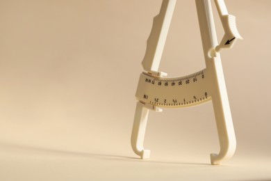 Photo of Plastic body fat caliper on beige background, closeup. Space for text