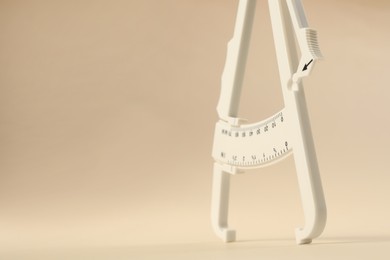 Photo of Plastic body fat caliper on beige background, closeup. Space for text