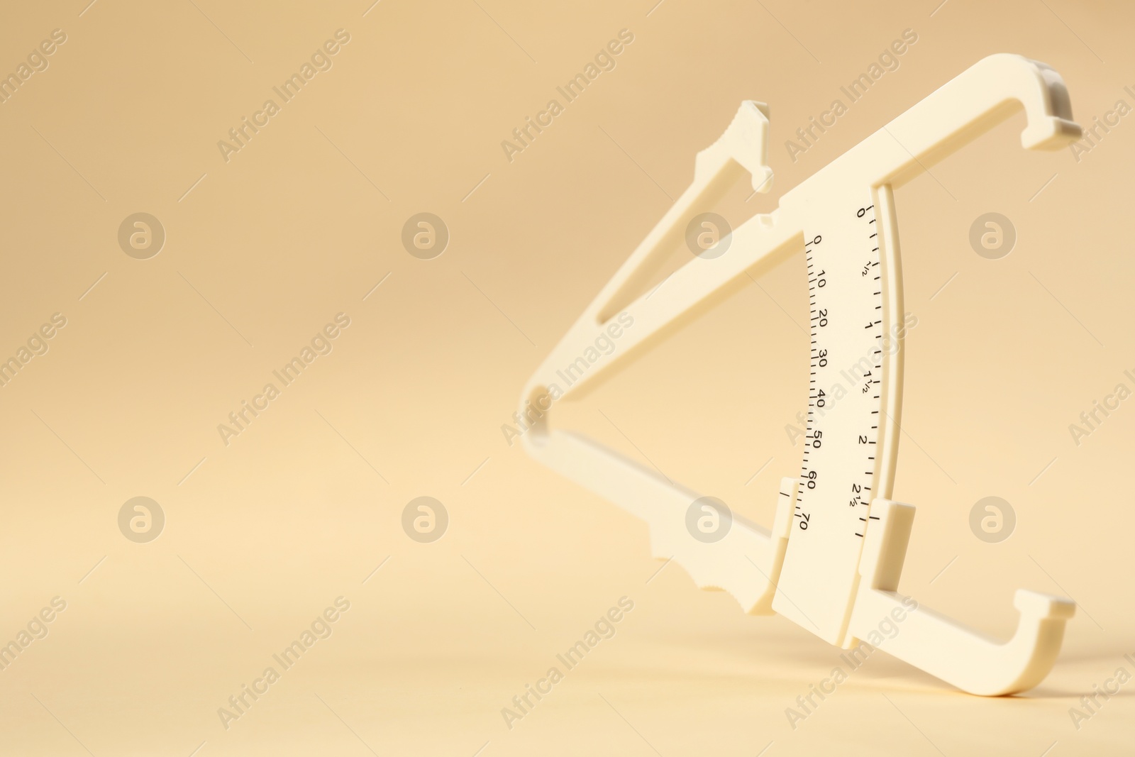 Photo of Plastic body fat caliper on beige background, closeup. Space for text