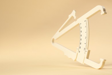 Photo of Plastic body fat caliper on beige background, closeup. Space for text