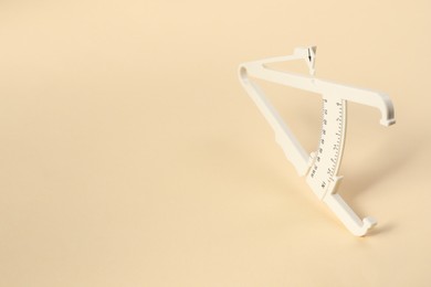 Photo of Plastic body fat caliper on beige background. Space for text