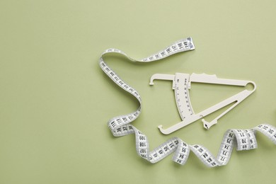 Photo of Body fat caliper and measuring tape on light green background, flat lay. Space for text