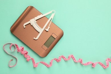 Photo of Body fat caliper, measuring tape and kitchen scale on turquoise background, flat lay. Space for text