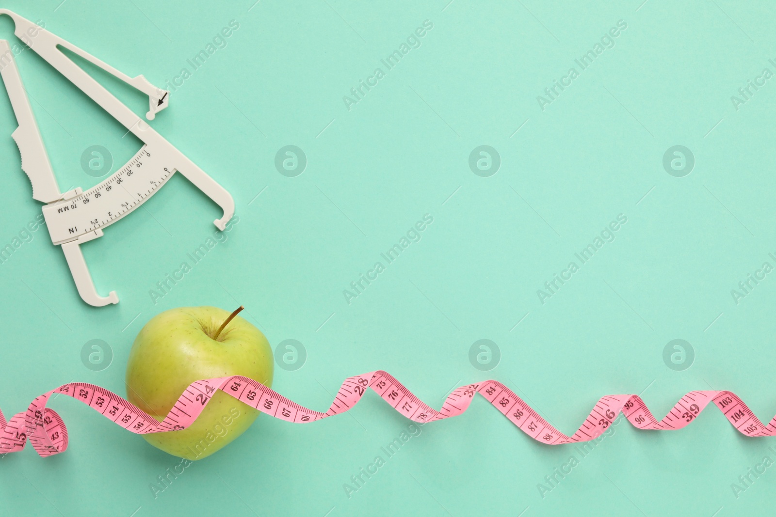 Photo of Body fat caliper, measuring tape and apple on turquoise background, flat lay. Space for text