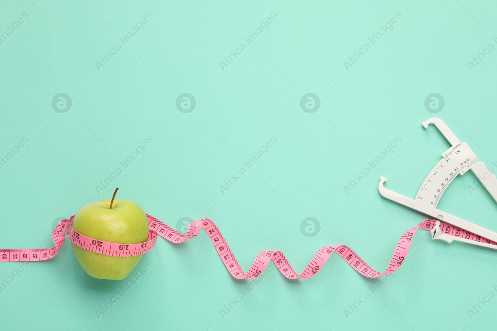 Photo of Body fat caliper, measuring tape and apple on turquoise background, flat lay. Space for text