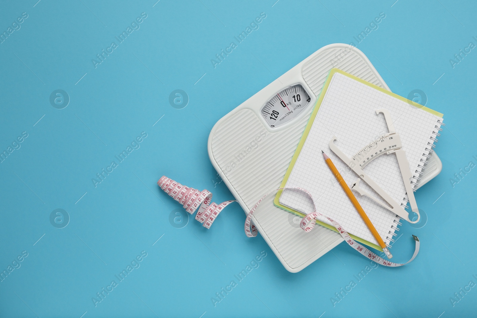 Photo of Body fat caliper, measuring tape, scale and notebook on light blue background, top view. Space for text