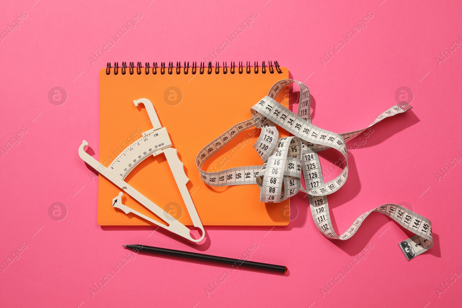 Photo of Body fat caliper, measuring tape, notebook and pencil on pink background, flat lay