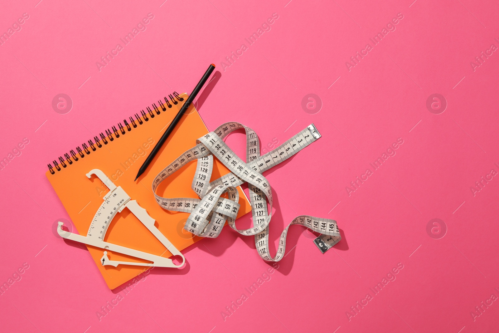 Photo of Body fat caliper, measuring tape, notebook and pencil on pink background, flat lay. Space for text