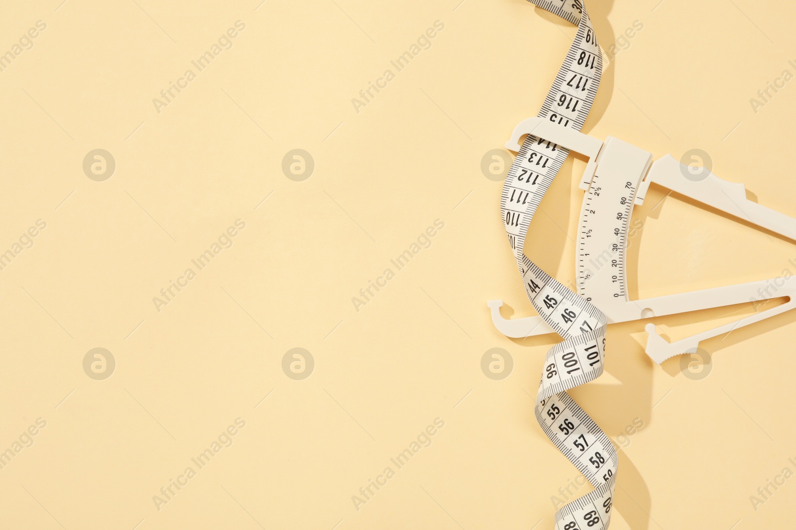 Photo of Plastic body fat caliper and measuring tape on beige background, top view. Space for text