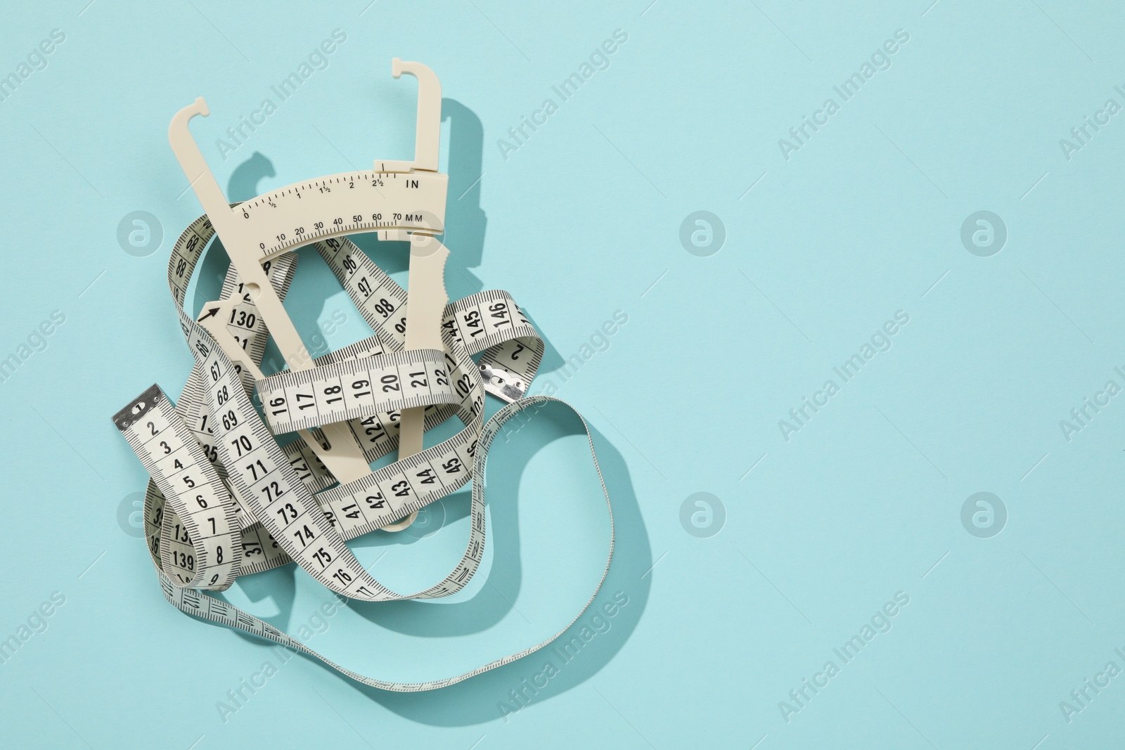 Photo of Plastic body fat caliper and measuring tape on light blue background, top view. Space for text