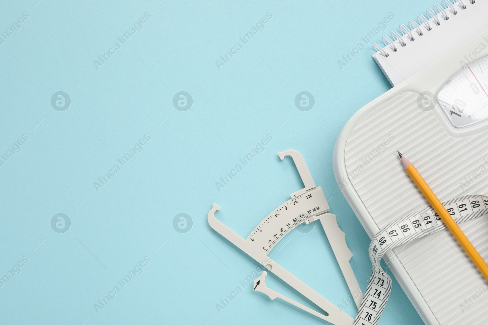 Photo of Body fat caliper, measuring tape, scale, pencil and notebook on light blue background, flat lay. Space for text