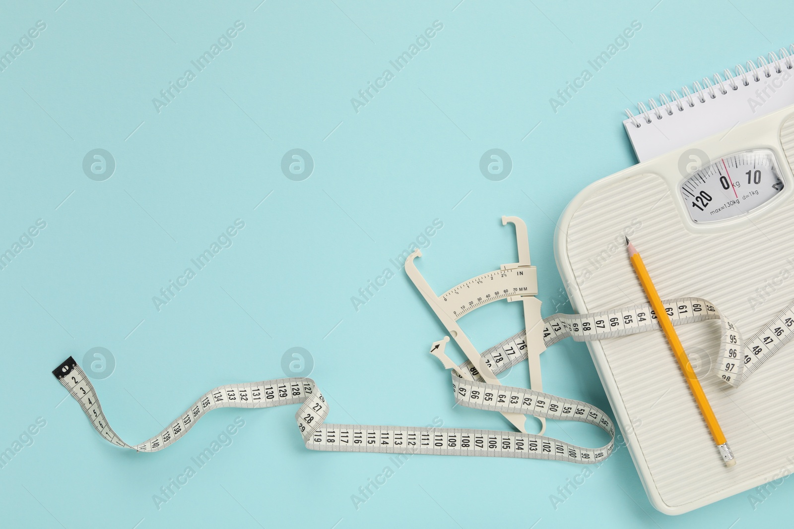 Photo of Body fat caliper, measuring tape, scale, pencil and notebook on light blue background, flat lay. Space for text