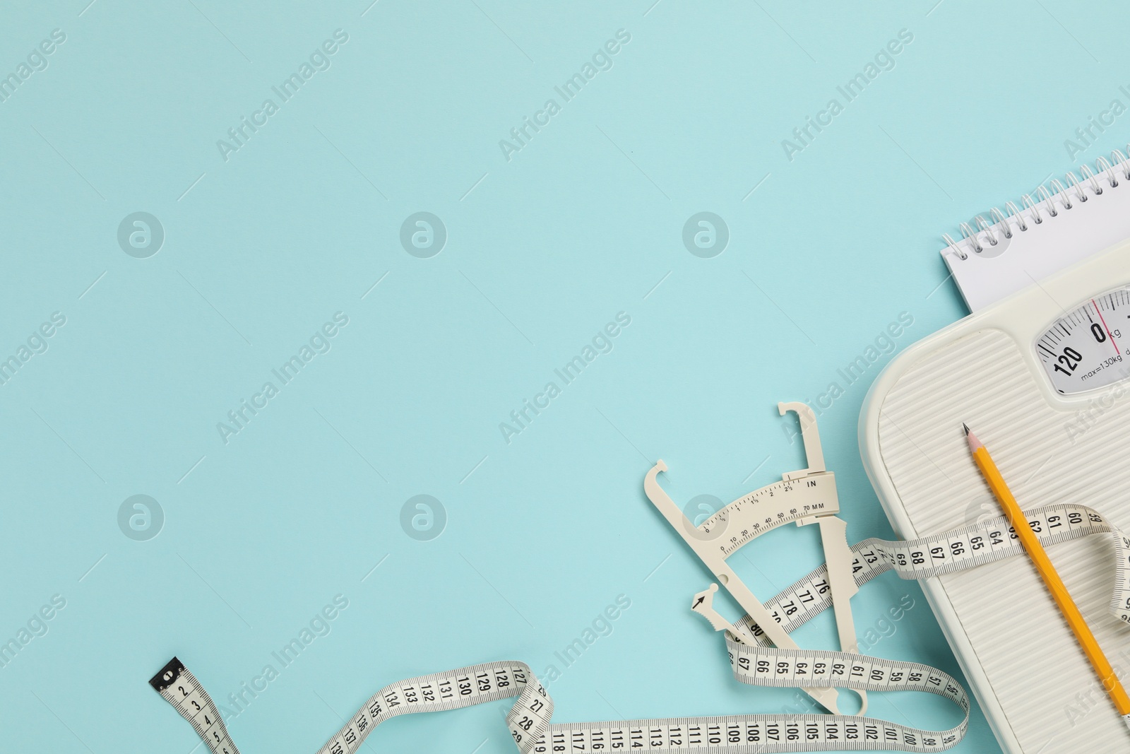 Photo of Body fat caliper, measuring tape, scale, pencil and notebook on light blue background, flat lay. Space for text