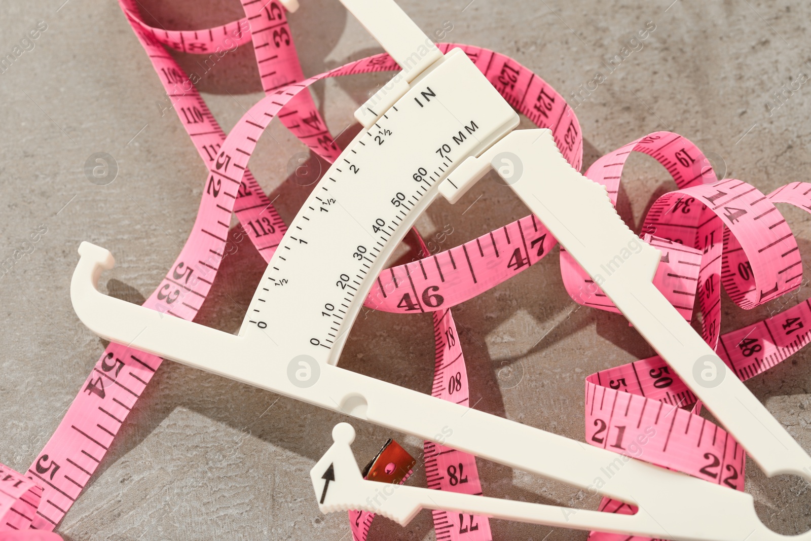 Photo of Plastic body fat caliper and measuring tape on grey table, closeup